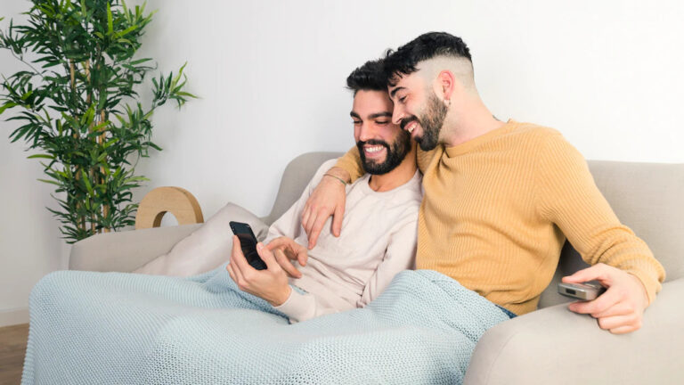 pareja-gay-joven-feliz-sentados-juntos-sofa-mirando-telefono-movil_23-2148083034